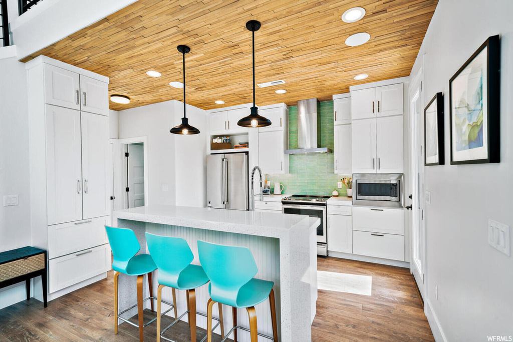 Kitchen with wall chimney range hood, white cabinets, stainless steel appliances, and backsplash