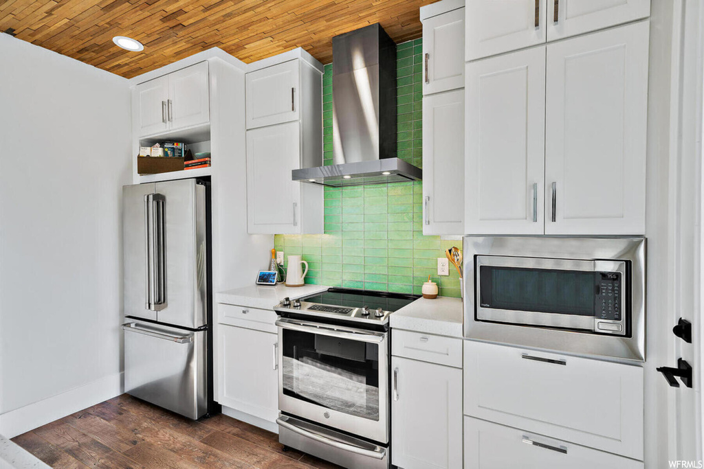 Kitchen with dark hardwood / wood-style flooring, wall chimney range hood, wooden ceiling, stainless steel appliances, and backsplash