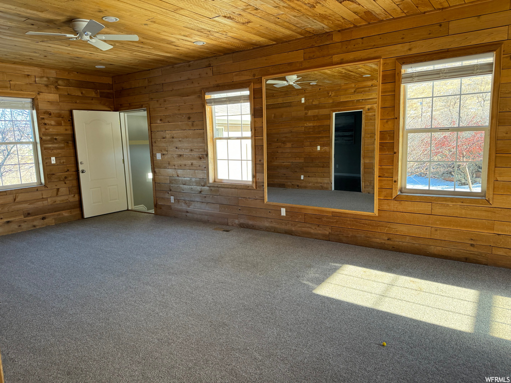 Spare room featuring dark colored carpet, wood ceiling, ceiling fan, and plenty of natural light