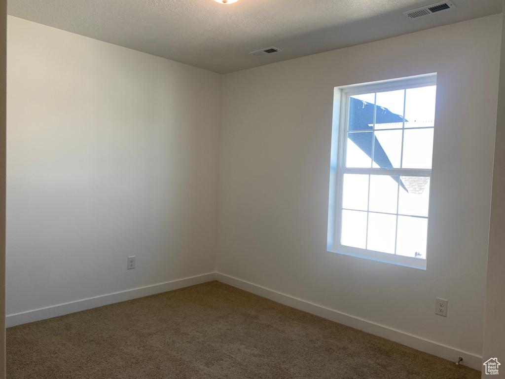 Unfurnished room featuring a textured ceiling, dark colored carpet, and a healthy amount of sunlight