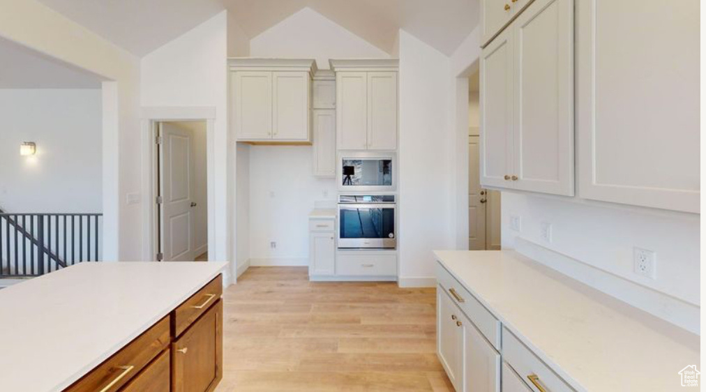 Kitchen with built in microwave, light wood-type flooring, stainless steel oven, and white cabinetry