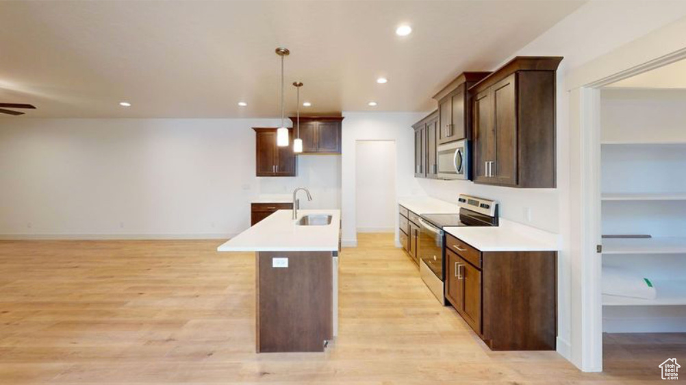 Kitchen featuring light hardwood / wood-style flooring, stainless steel appliances, sink, ceiling fan, and an island with sink