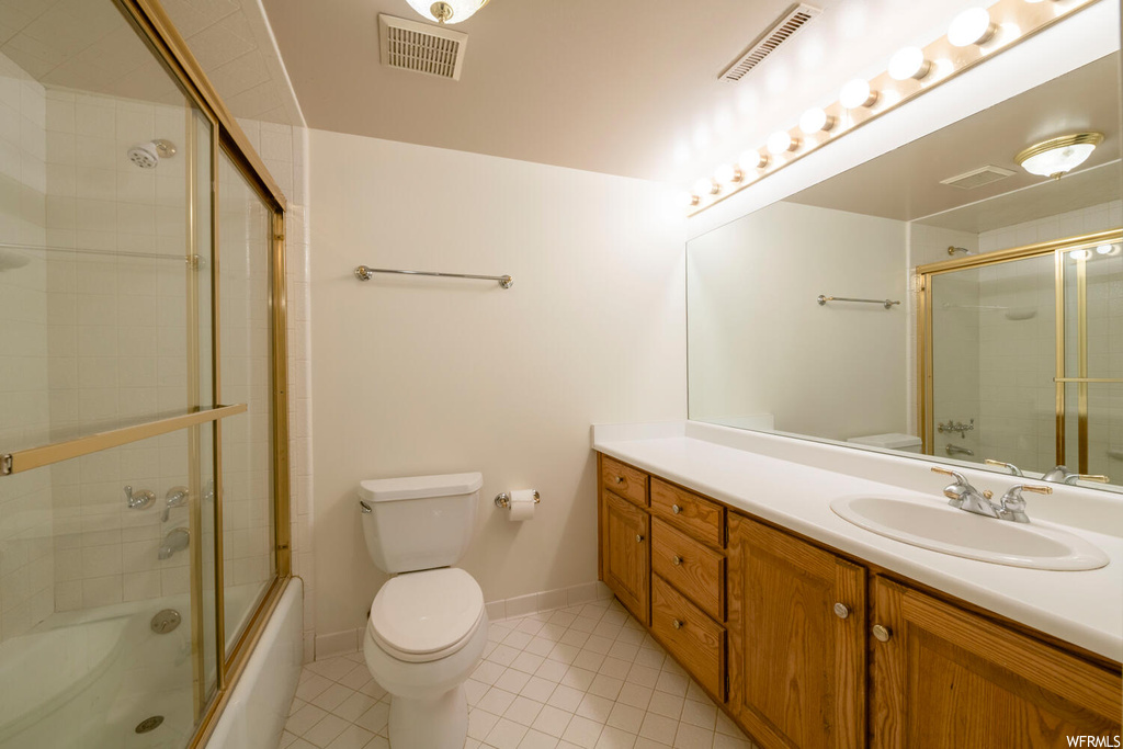 Full bathroom with bath / shower combo with glass door, toilet, tile floors, and vanity with extensive cabinet space