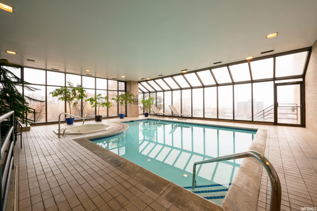 View of pool featuring a jacuzzi, a patio area, and glass enclosure