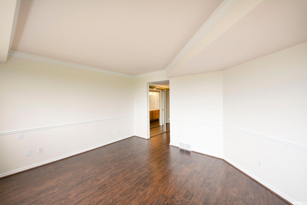 Empty room featuring dark wood-type flooring and crown molding