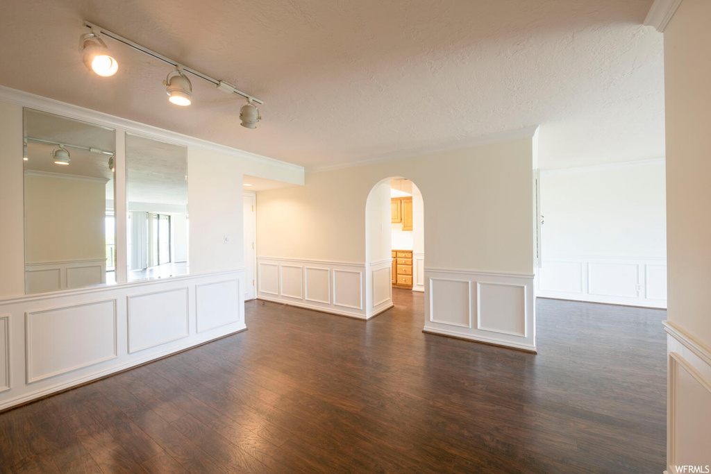 Empty room featuring ornamental molding, dark wood-type flooring, and rail lighting