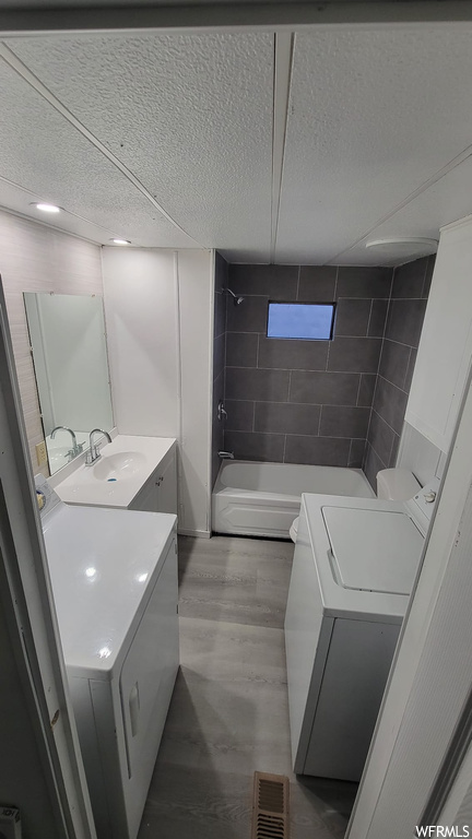 Full bathroom featuring toilet, tub / shower combination, separate washer and dryer, vanity with extensive cabinet space, and hardwood / wood-style floors