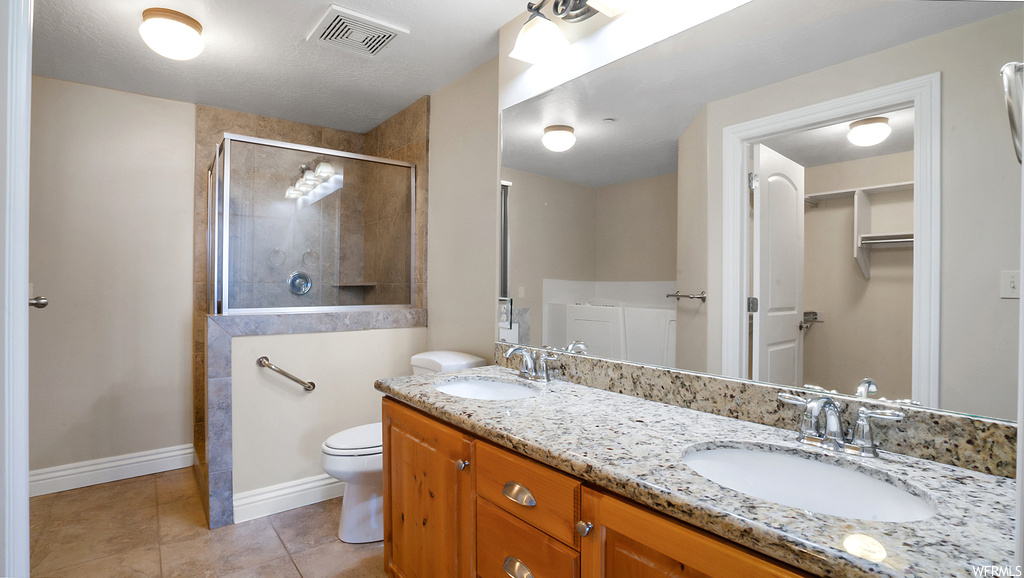 Bathroom featuring dual sinks, a shower with shower door, tile flooring, toilet, and vanity with extensive cabinet space