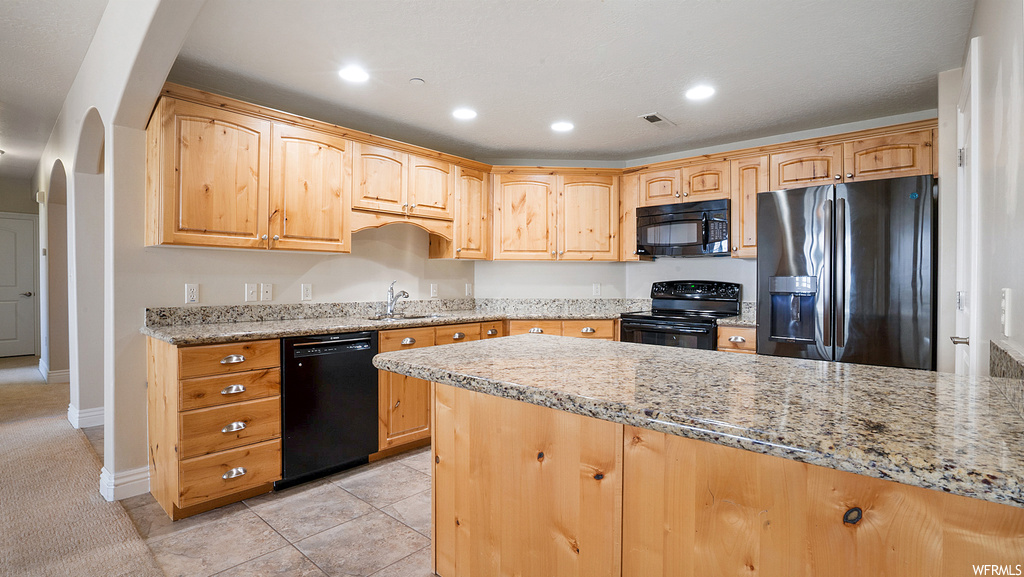Kitchen featuring light tile flooring, sink, light stone countertops, black appliances, and kitchen peninsula
