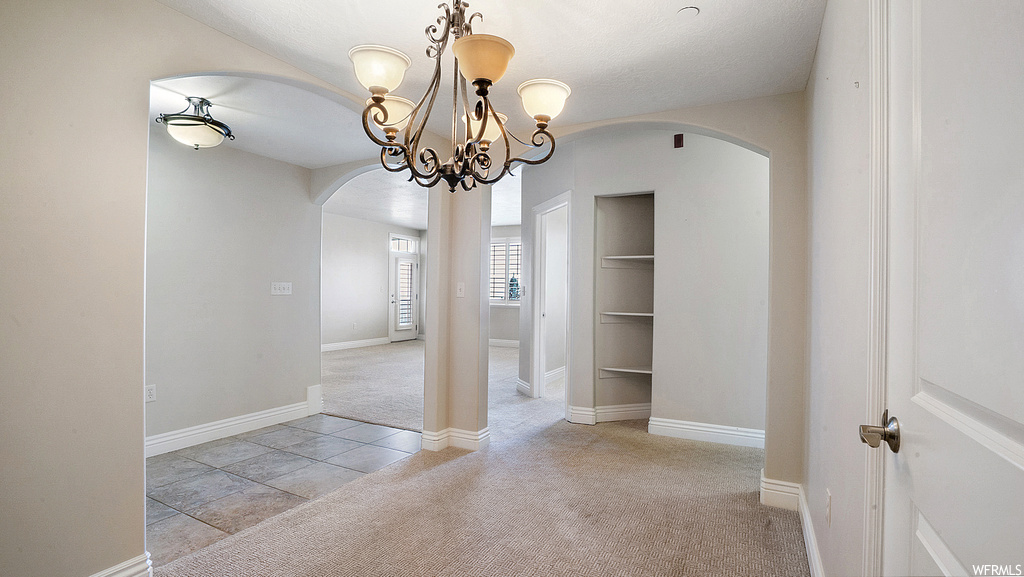 Empty room featuring light tile floors and a notable chandelier