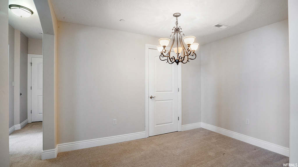 Carpeted empty room featuring an inviting chandelier