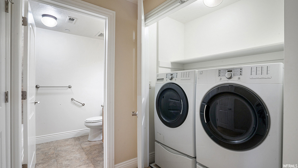 Clothes washing area with light tile flooring and washing machine and dryer