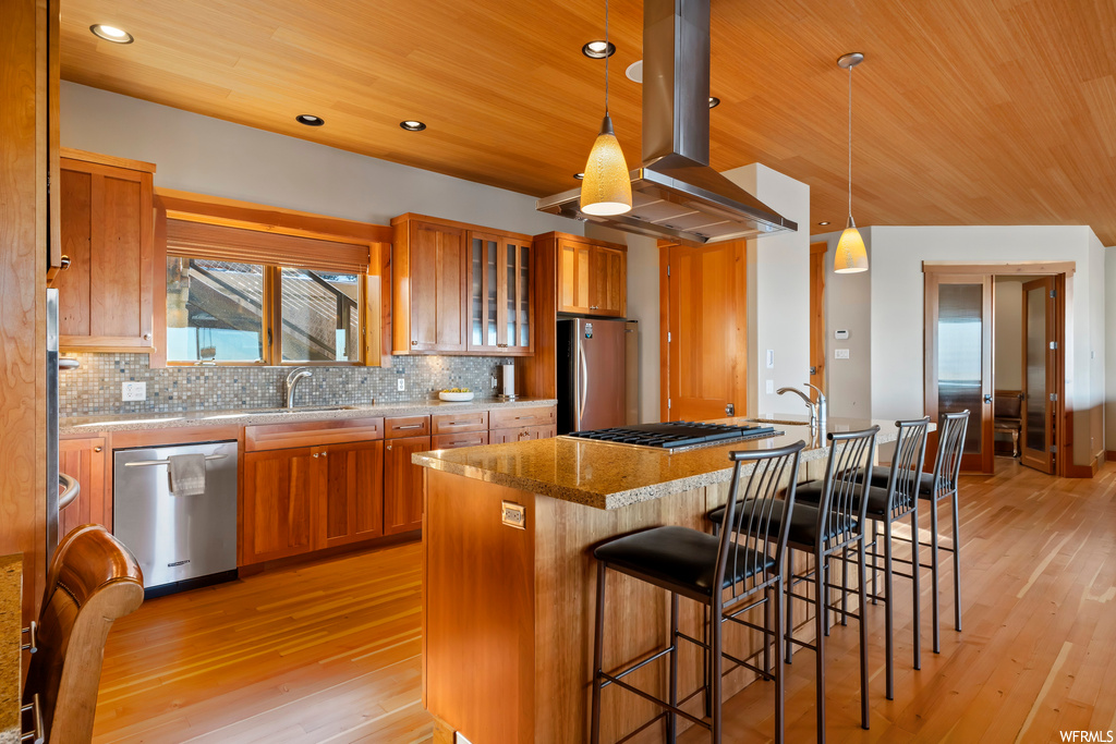 Kitchen featuring island exhaust hood, hanging light fixtures, appliances with stainless steel finishes, and light hardwood / wood-style floors
