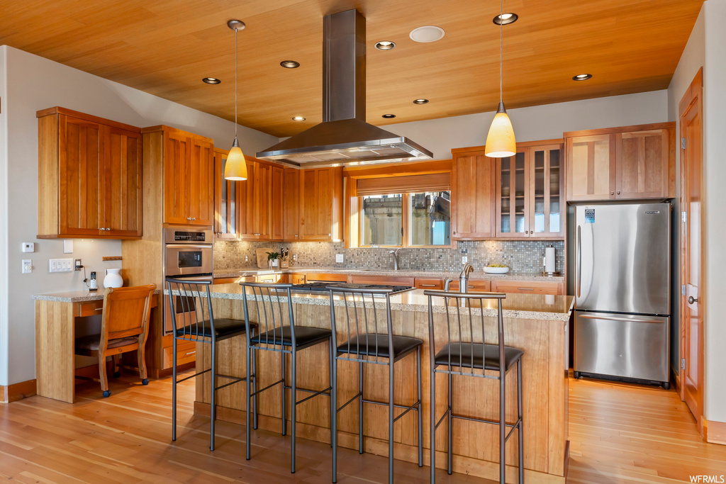 Kitchen featuring a center island, island exhaust hood, light hardwood / wood-style floors, stainless steel appliances, and decorative light fixtures