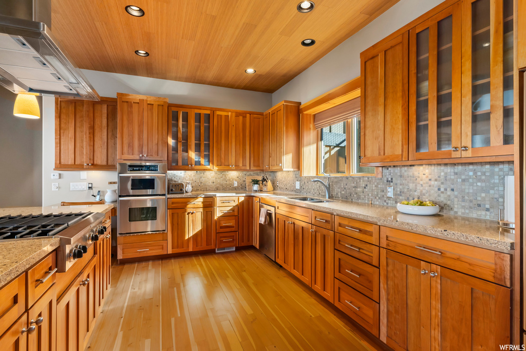 Kitchen with sink, light stone counters, light wood-type flooring, tasteful backsplash, and range hood