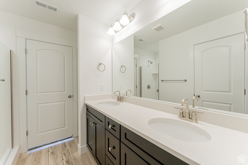 Bathroom featuring wood-type flooring, oversized vanity, walk in shower, and dual sinks