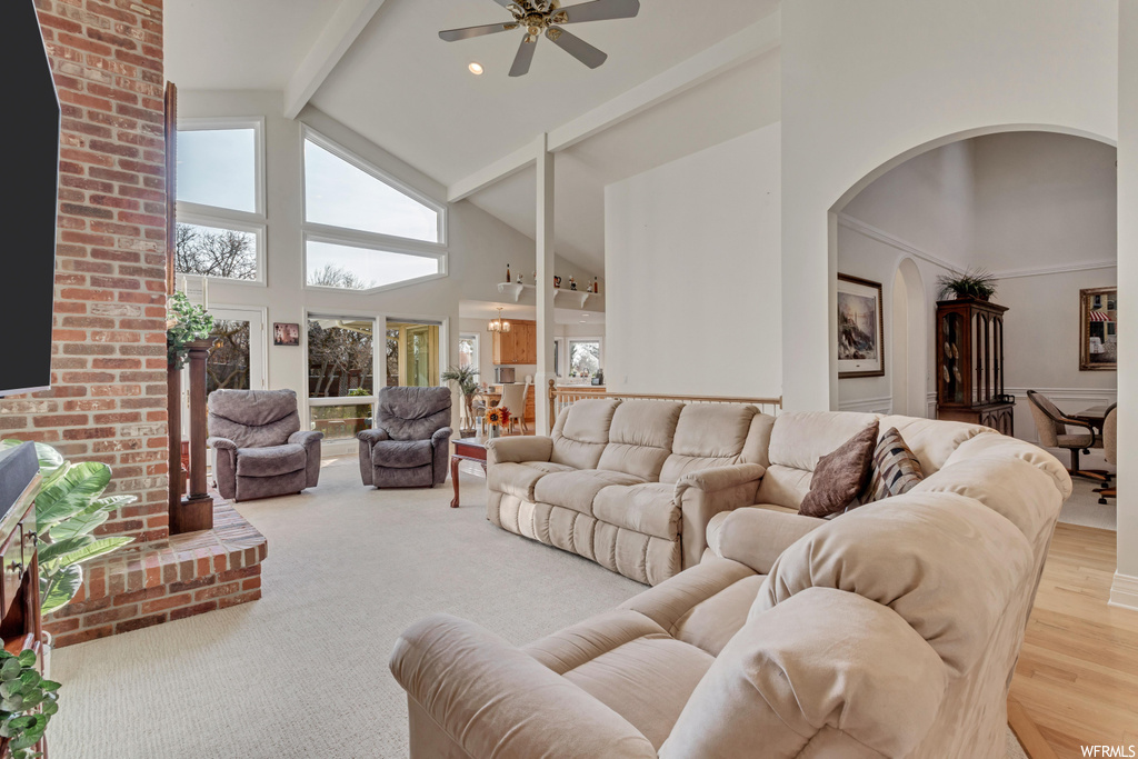 Living room featuring beamed ceiling, high vaulted ceiling, ceiling fan, brick wall, and light carpet