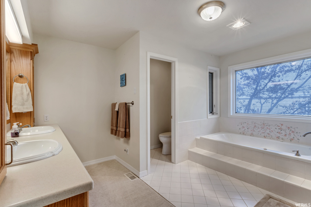 Bathroom featuring tiled bath, toilet, double sink, and tile floors