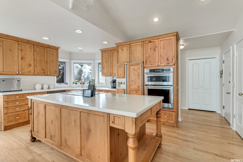 Kitchen featuring sink, double oven, light hardwood / wood-style floors, lofted ceiling, and a kitchen island