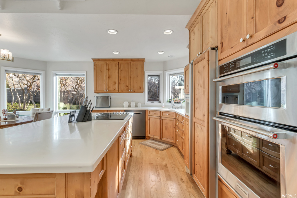 Kitchen featuring an inviting chandelier, pendant lighting, stainless steel appliances, light hardwood / wood-style flooring, and a kitchen island