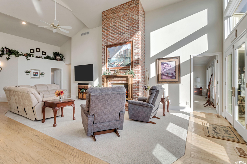 Living room with high vaulted ceiling, ceiling fan, a fireplace, and brick wall