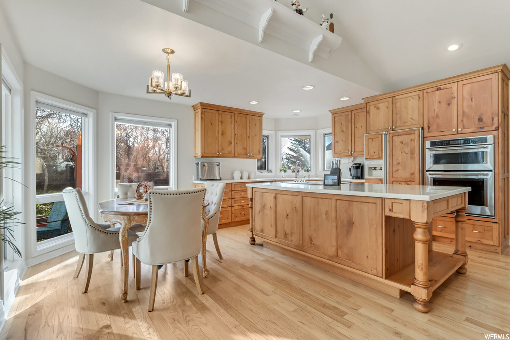 Kitchen featuring a center island, light hardwood / wood-style flooring, a healthy amount of sunlight, stainless steel double oven, and decorative light fixtures