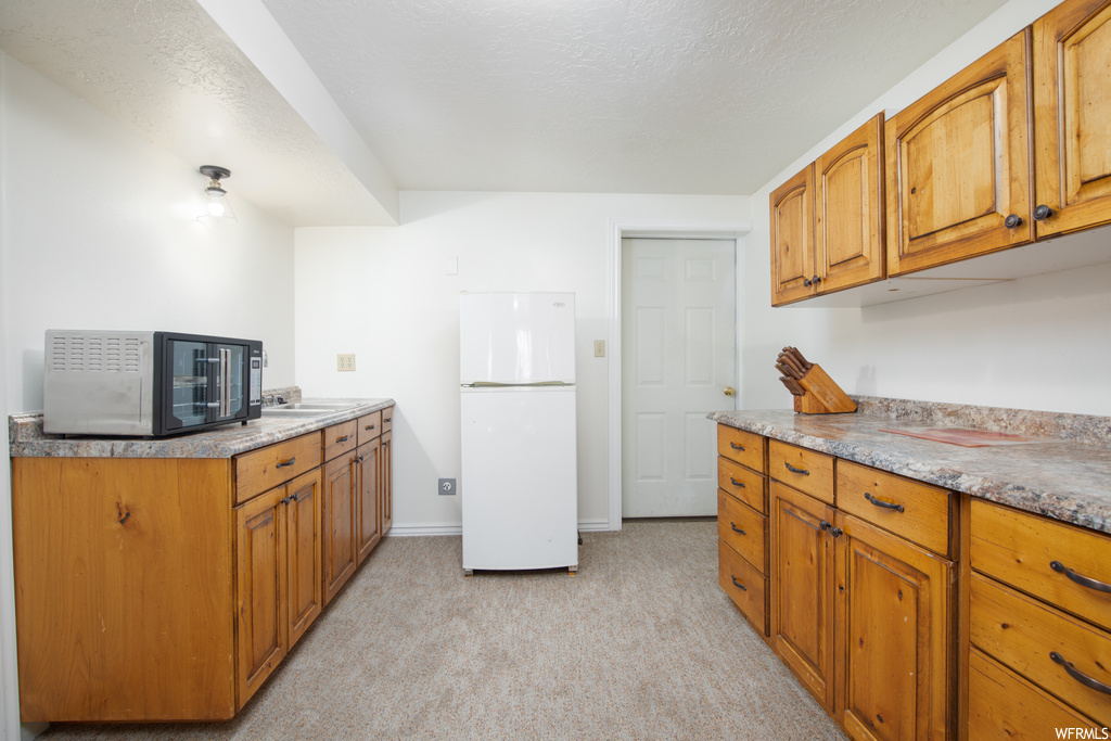 Kitchen featuring white refrigerator, sink, and light colored carpet