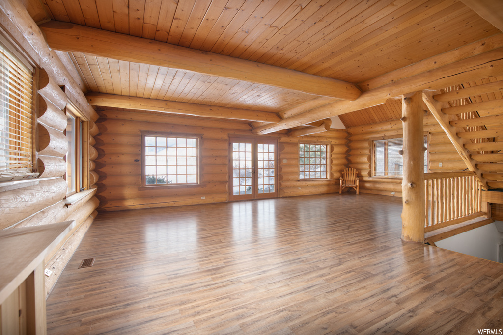 Unfurnished living room featuring wood ceiling, beamed ceiling, rustic walls, and hardwood / wood-style flooring