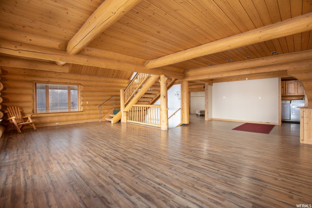 Unfurnished living room featuring wood-type flooring, log walls, beam ceiling, and wooden ceiling