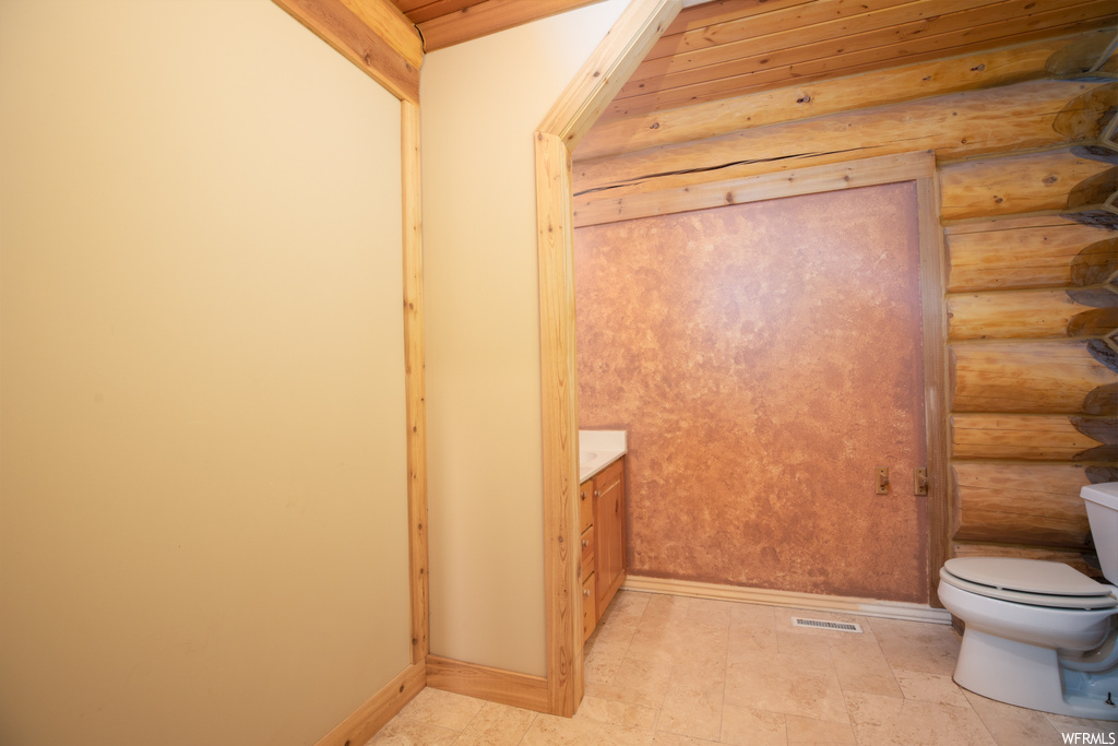 Bathroom with wood ceiling, vanity, rustic walls, toilet, and tile floors