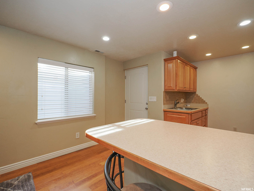 Kitchen featuring light brown cabinets, sink, a kitchen breakfast bar, light hardwood / wood-style floors, and backsplash
