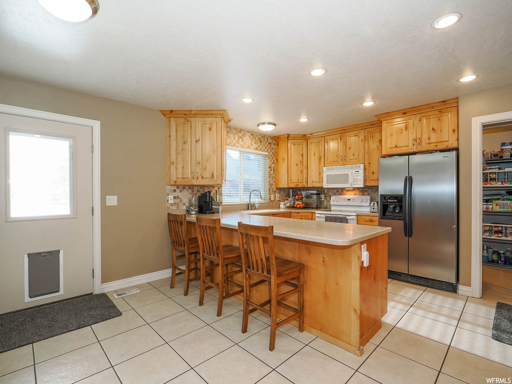 Kitchen with white appliances, light tile flooring, a kitchen breakfast bar, and backsplash