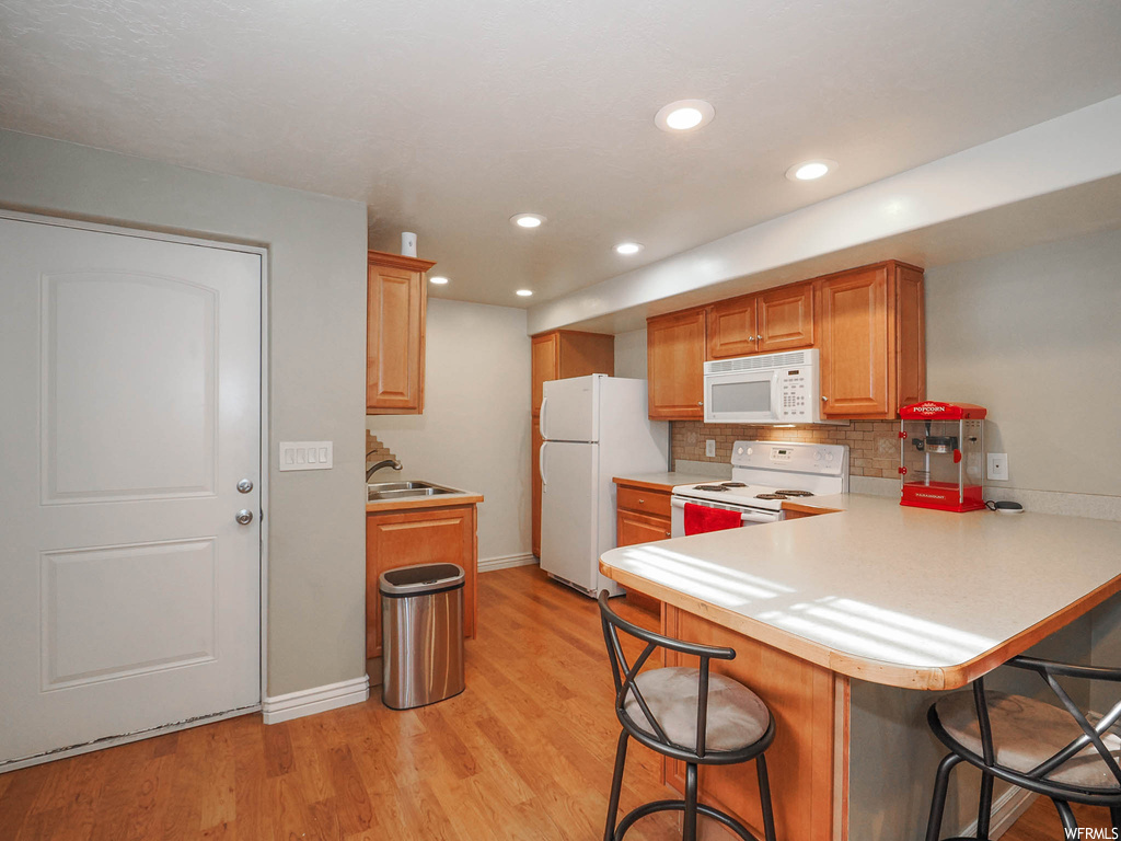 Kitchen with white appliances, backsplash, light wood-type flooring, and kitchen peninsula