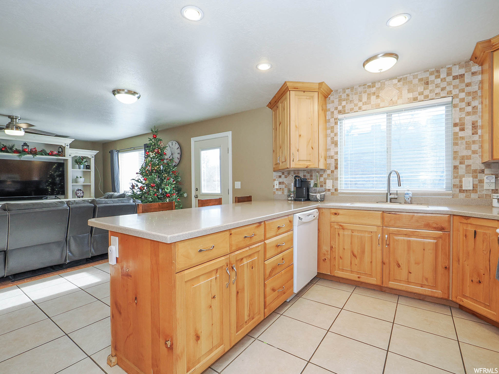 Kitchen featuring backsplash, light tile floors, dishwasher, and kitchen peninsula