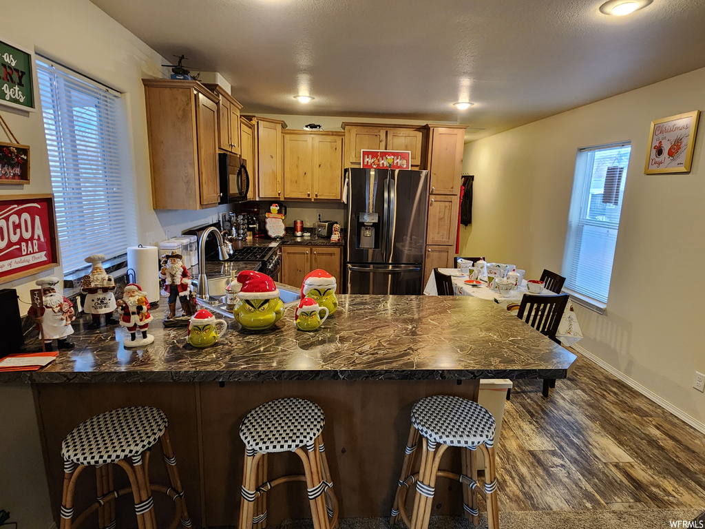 Kitchen with dark hardwood / wood-style flooring, a healthy amount of sunlight, kitchen peninsula, and stainless steel fridge with ice dispenser
