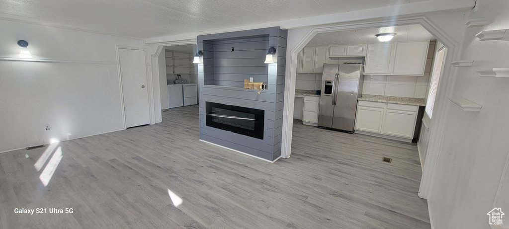 Kitchen with stainless steel fridge, white cabinets, separate washer and dryer, tasteful backsplash, and light hardwood / wood-style floors
