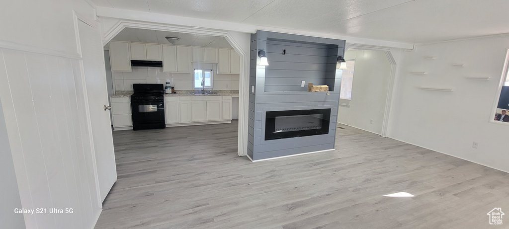 Kitchen featuring light wood-type flooring, black range, backsplash, and sink