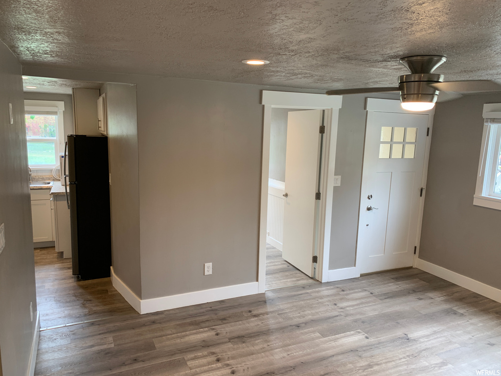 Unfurnished bedroom with a textured ceiling, connected bathroom, black fridge, light wood-type flooring, and ceiling fan