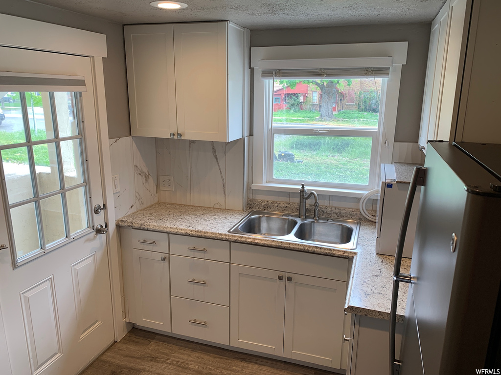 Kitchen featuring sink, hardwood / wood-style flooring, stainless steel fridge, white cabinets, and tasteful backsplash