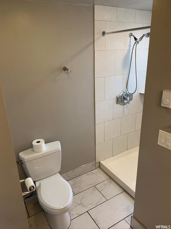Bathroom featuring toilet, tile flooring, and a tile shower