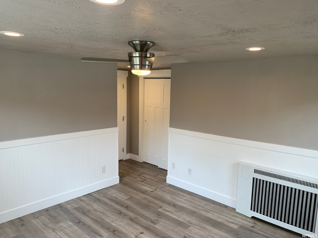 Unfurnished room featuring radiator, ceiling fan, a textured ceiling, and hardwood / wood-style flooring