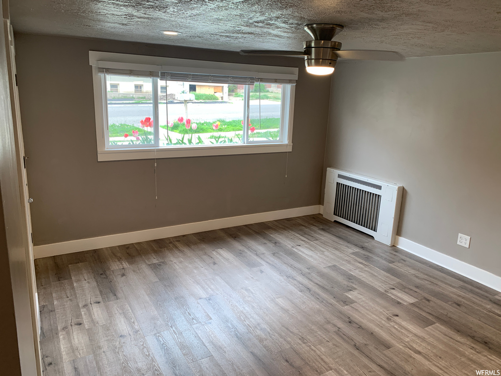 Spare room featuring radiator heating unit, light wood-type flooring, ceiling fan, and a textured ceiling