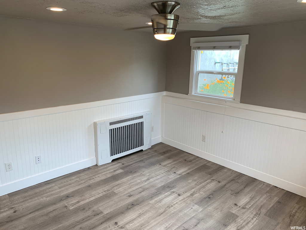 Unfurnished room with ceiling fan, a textured ceiling, radiator, and hardwood / wood-style flooring