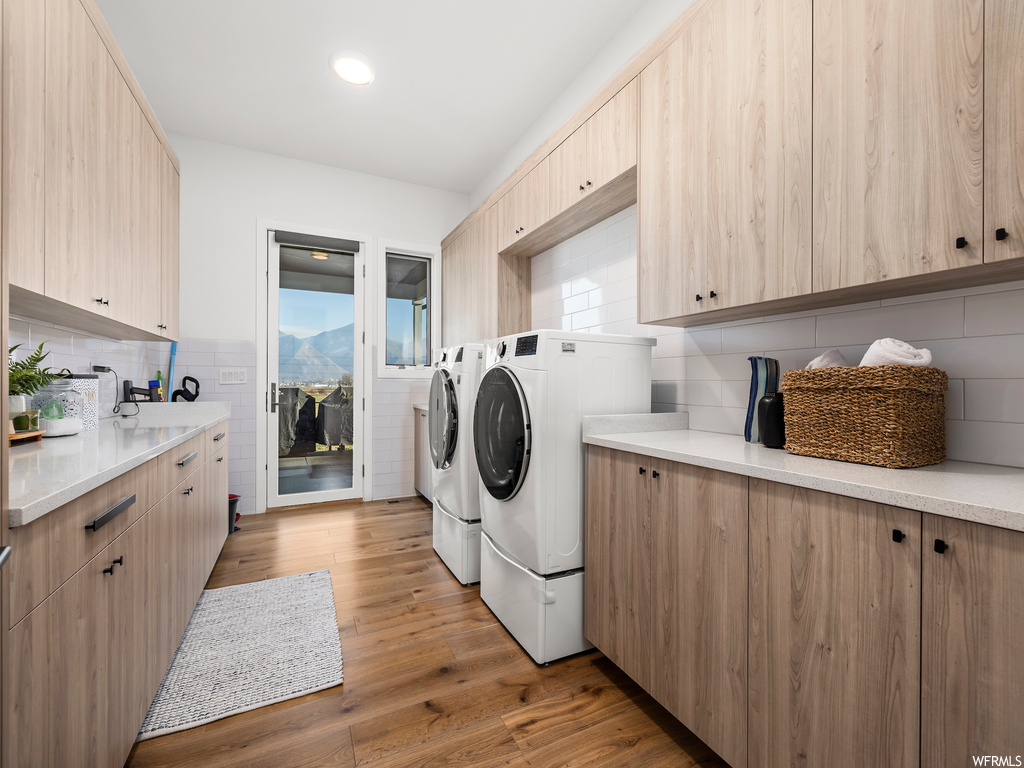 Clothes washing area with washer and clothes dryer, cabinets, and light hardwood / wood-style floors