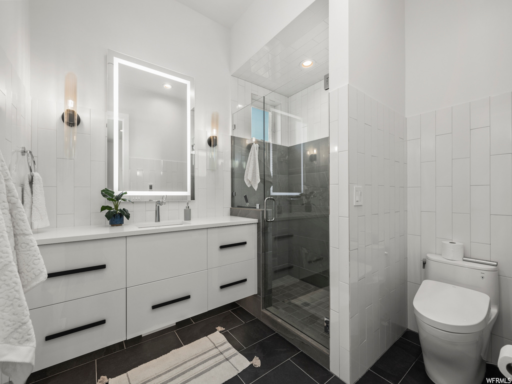 Bathroom with tile flooring, tile walls, a shower with shower door, and vanity