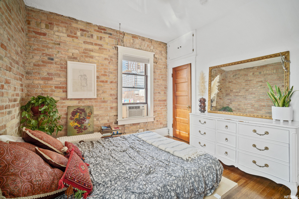 Bedroom with dark hardwood / wood-style floors and brick wall