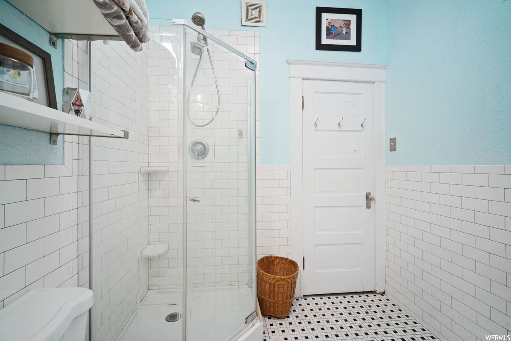 Bathroom featuring toilet, tile floors, tile walls, and a shower with shower door