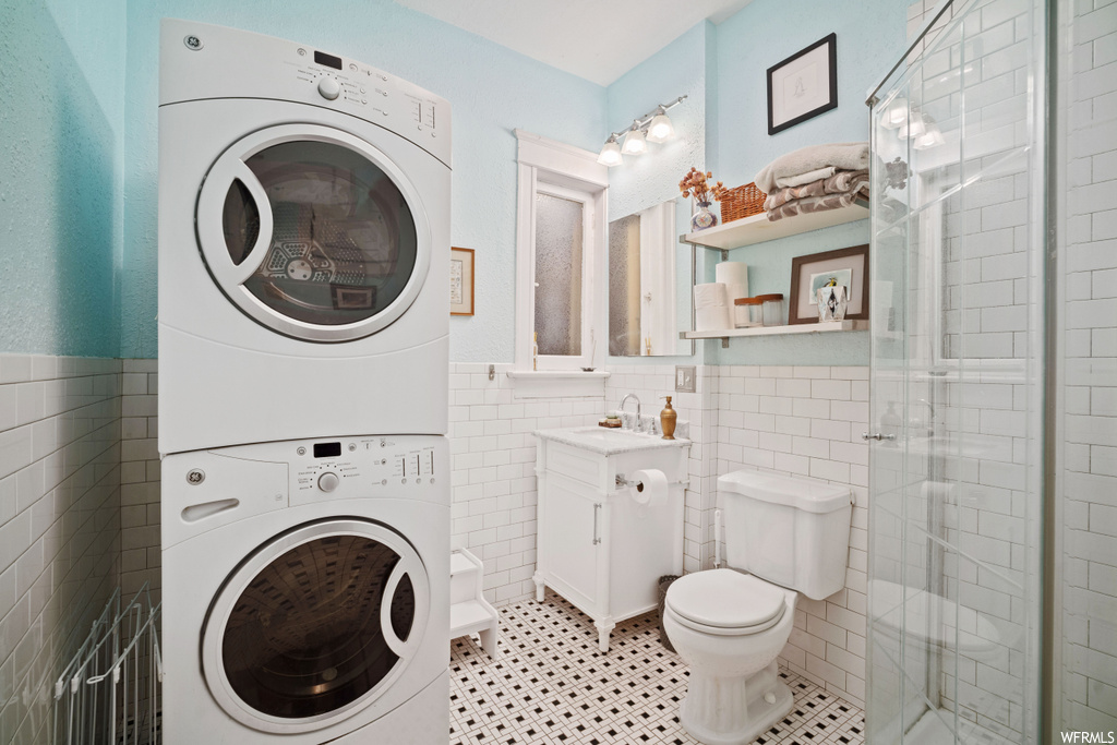 Washroom with stacked washer and clothes dryer, tile walls, sink, and light tile floors