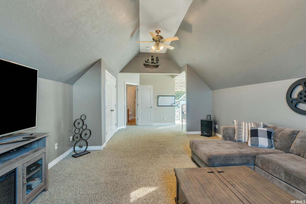 Carpeted living room with lofted ceiling, ceiling fan, and a textured ceiling