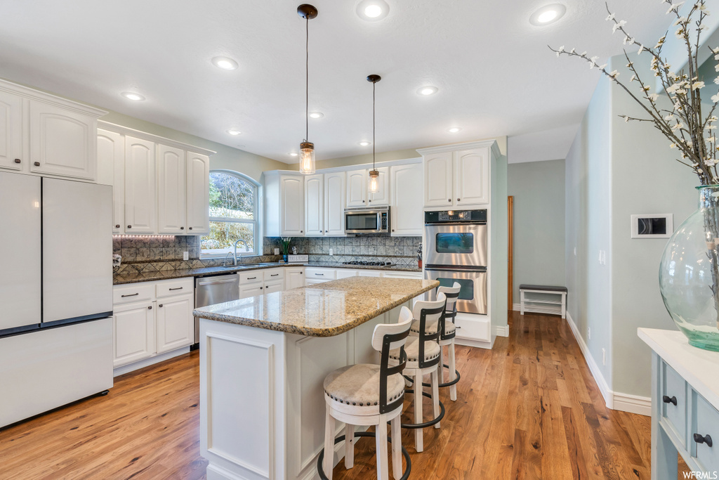 Kitchen featuring hanging light fixtures, appliances with stainless steel finishes, backsplash, light hardwood / wood-style flooring, and white cabinetry